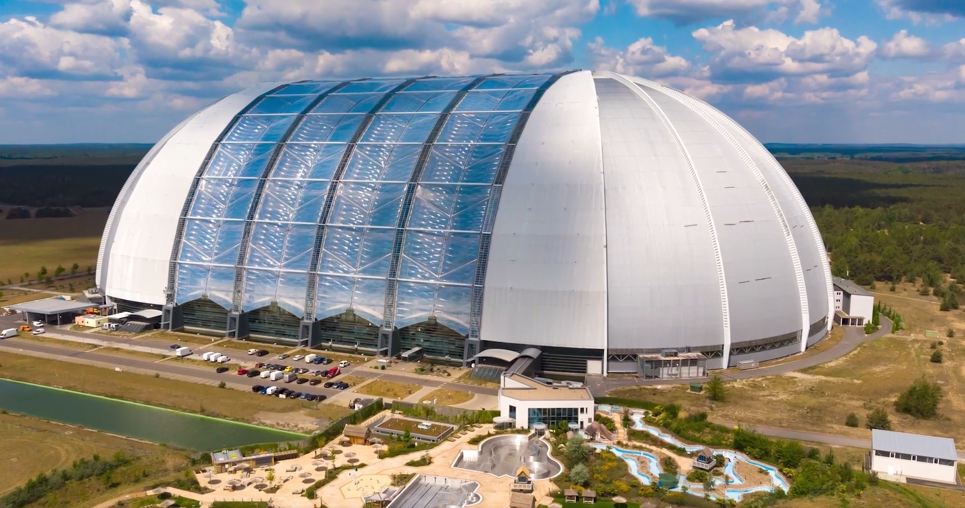 Scena przedstawia zdjęcia zlokalizowanego pod olbrzymią kopułą parku Tropical Island. W jej wnętrzu stworzono park tropikalny. Obok pojawia się napis: Tropical Island ist ein großartiger Ort für Wasserratten. 