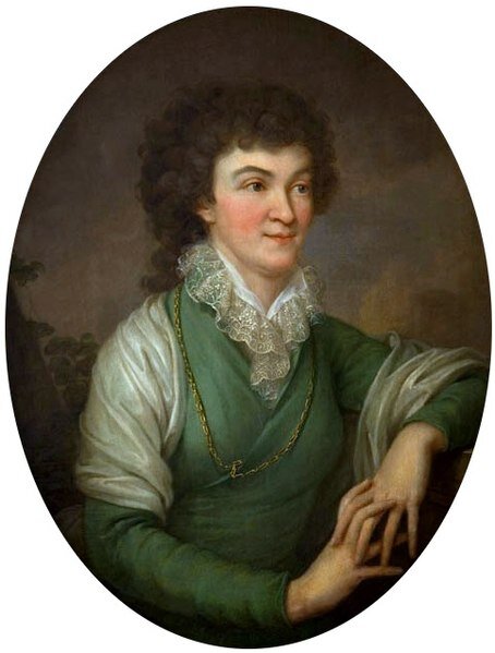 Ilustracja przedstawia portret kobiety z długimi kręconymi włosami zaczesanymi do tyłu. Jest ubrana w sukienkę spod której wystaje koronkowy kołnierz, na ramionach ma zarzuconą chustę, na szyi wisi łańcuch. Kobieta ma splecione dłonie, jeden łokieć opiera o oparcie krzesła.