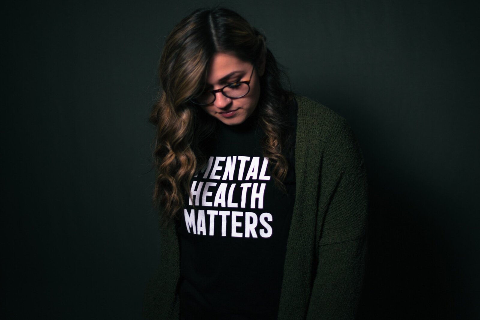 Zdjęcie przedstawia młodą kobietę z pochyloną głową. Ubrana jest w czarną koszulkę z białym napisem w języku angielskim:  MENTAL HEALTH MATTERS. Transkrypcja znajduje się poniżej.