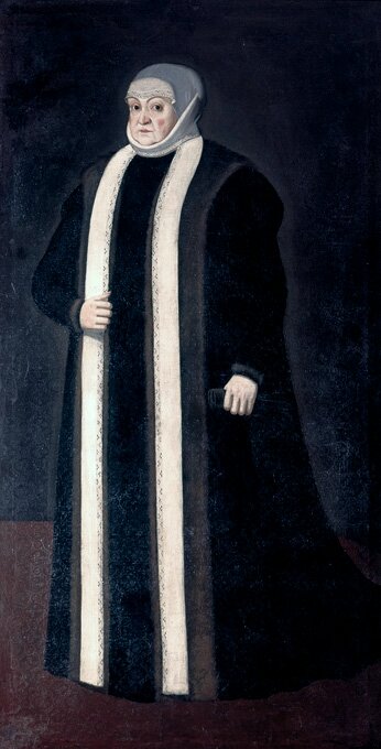 Na ilustracji portret jest królowej Bony. Królowa jest korpulentna. Ubrana jest w długi do ziemi, czarny płaszcz z białą szeroką lamówką. Prawą dłoń trzyma za lamówką na wysokości pasa. W lewej dłoni trzyma ciemne rękawiczki. Płaszcz zakrywa ręce, szyję królowej. Na głowie ma szarą chustkę, która okala czoło i szyję. Spod chusty wystaje wyszywany materiał, który zakrywa czoło. Królowa ma ciemne oczy, poważną twarz oraz różowe policzki.