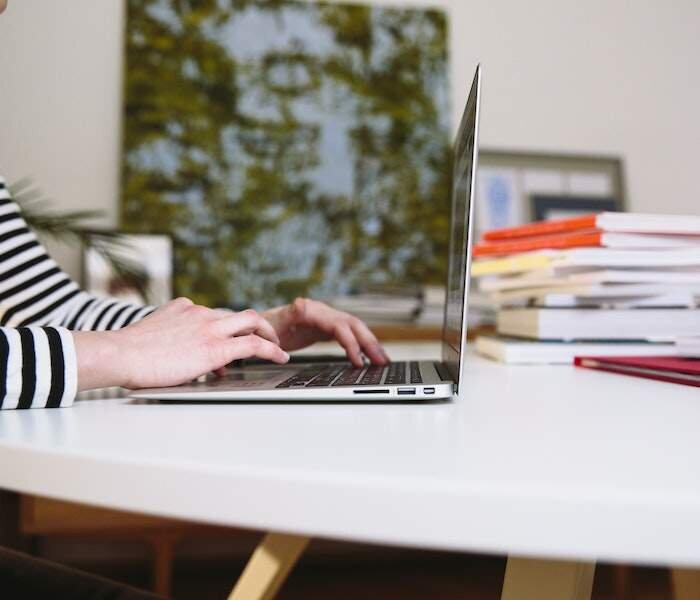 Zdjęcie piąte, podpisane Środki w zakresie edukacji i podjęcia pracy, przedstawia środki w zakresie edukacji i podjęcia pracy. Pokazany jest ustawiony na biurku otwarty laptop, na którym pracuje kobieta. Na biurku za laptopem leżą na stosie książki.