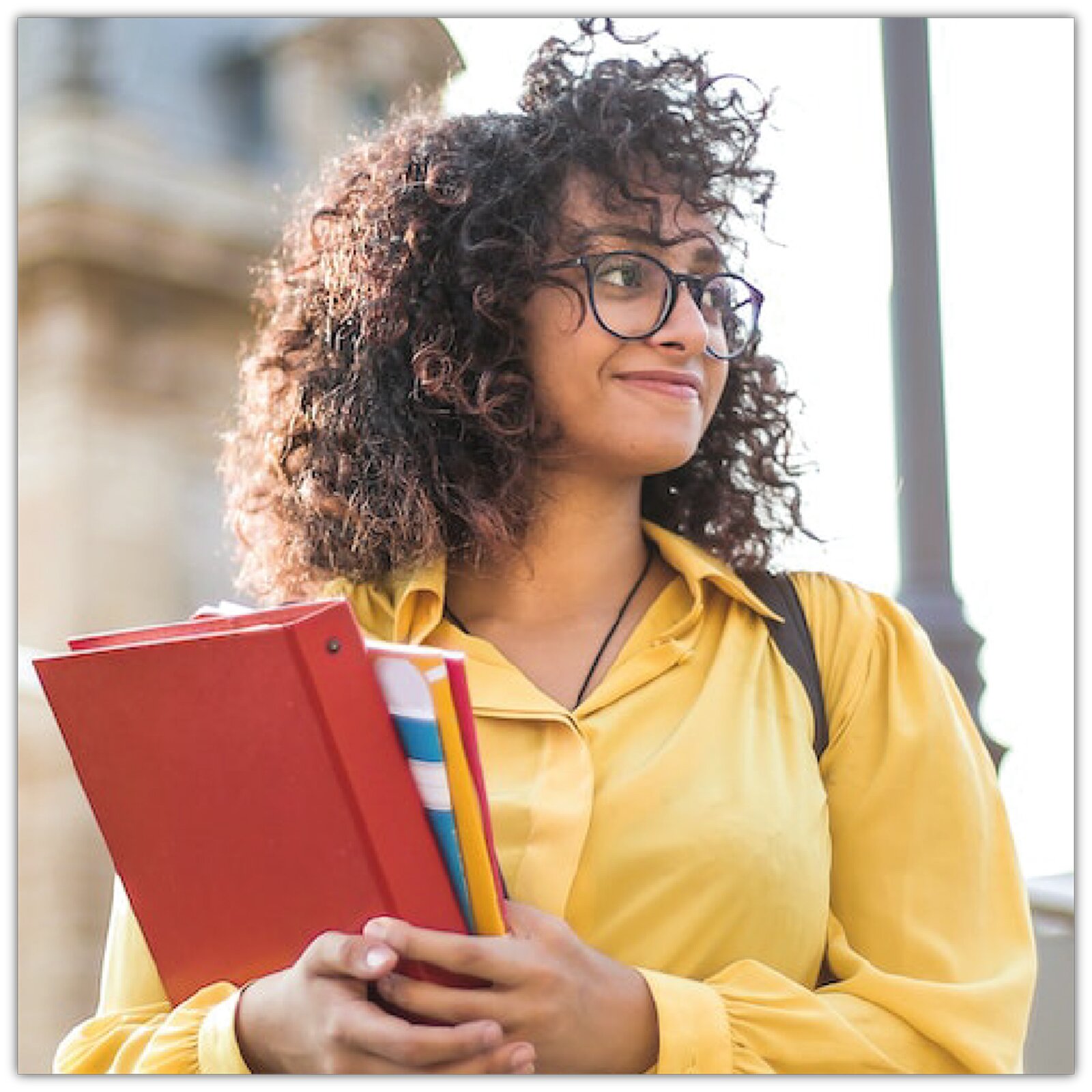 Zdjęcie przedstawia młodą dziewczynę w żółtej kurtce i okrągłych okularach korekcyjnych. Dziewczyna trzyma w ręku zeszyty. 
