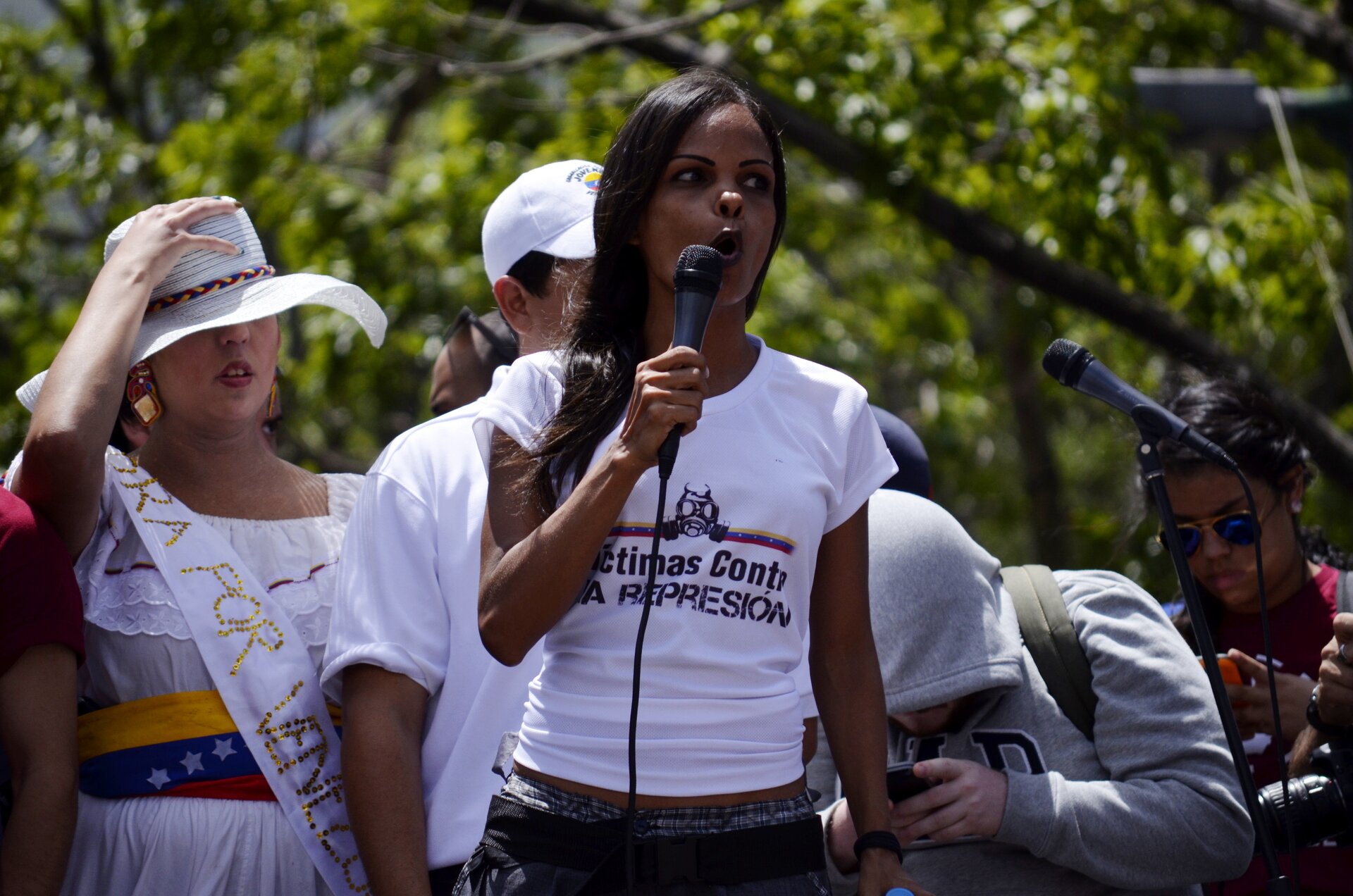 Na zdjęciu grupa ludzi, o różnych kolorach skóry, kobieta trzyma mikrofon.