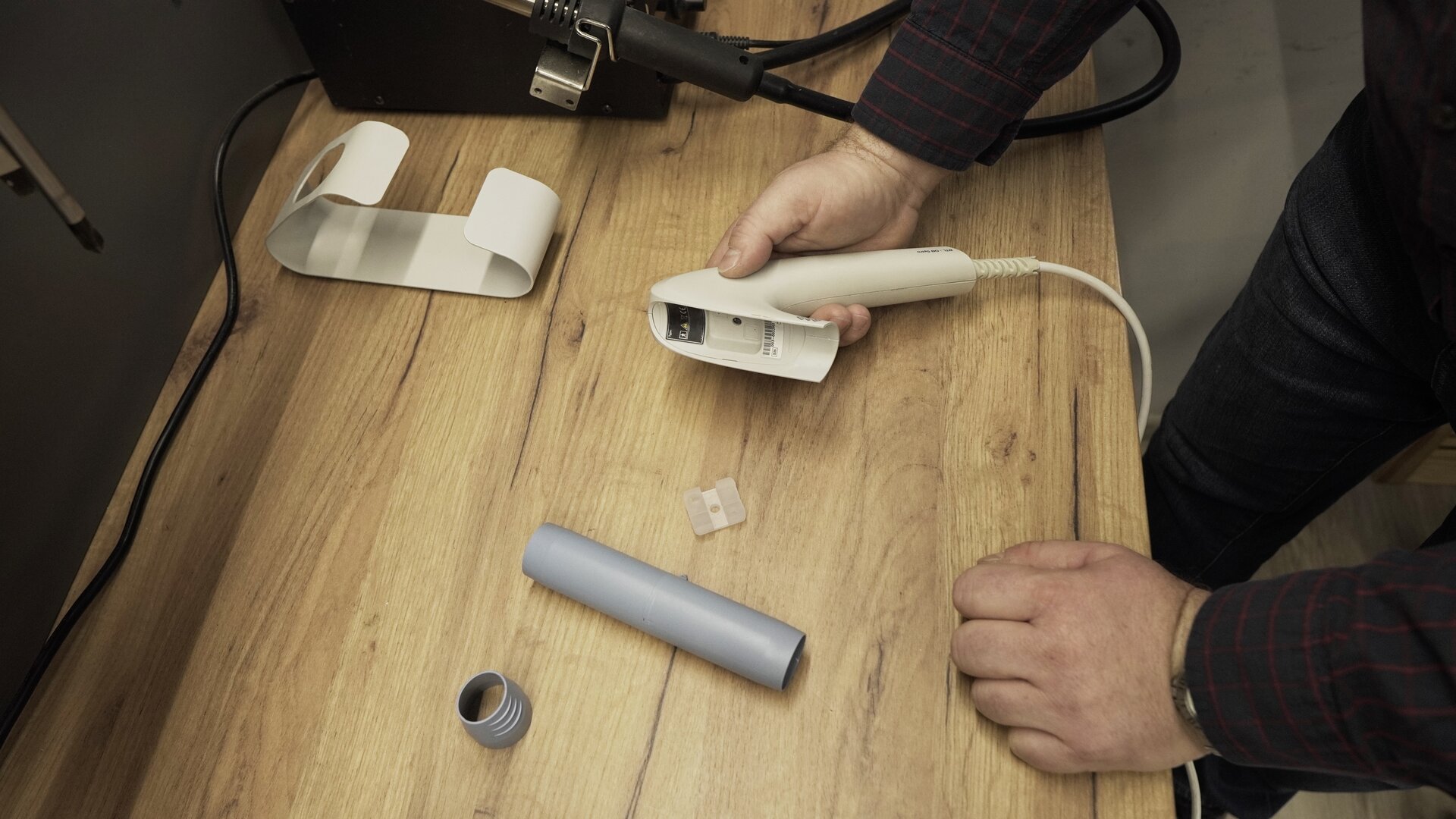 Na zdjęciu technik trzyma w ręku obudowę przetwornika spirometru. Na stole leżą: uszczelka przepływomierza, przepływomierz oraz ustnik.