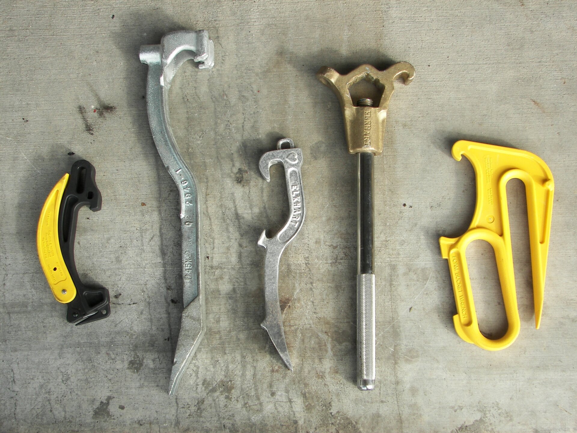 Na przedstawionym zdjęciu można zobaczyć kilka kluczy typu hakowego o różnych kształtach i rozmiarach. Pierwszy klucz posiada rękojeść w formie łuku, drugi jest długi i płaski, trzeci jest nieco mniejszy i wyposażony w szczękę w kształcie łuku, czwarty zaś jest sześciokątny i zakończony uchwytem. Ostatni klucz widoczny na zdjęciu jest wykonany z żeliwa.
