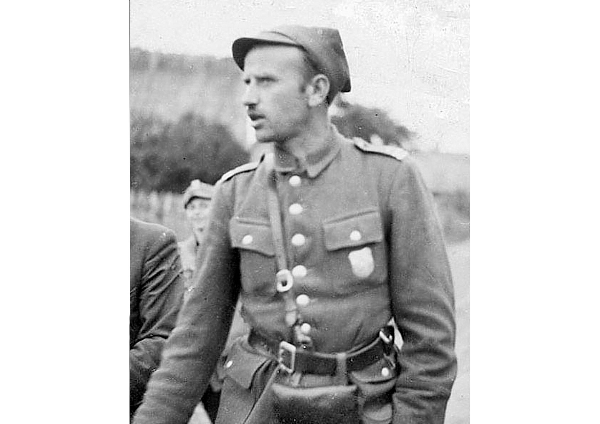 Fotografia portretowe Zygmunta Szendzielarza, pseudonim "Łupaszka". Mężczyzna w średnim wieku, ukazany do pasa. Twarz szczupła, włosy jasne, krótkie, wąsy. Ubrany w mundur polowy i rogatywkę. Zwrócony w lewą stronę. 