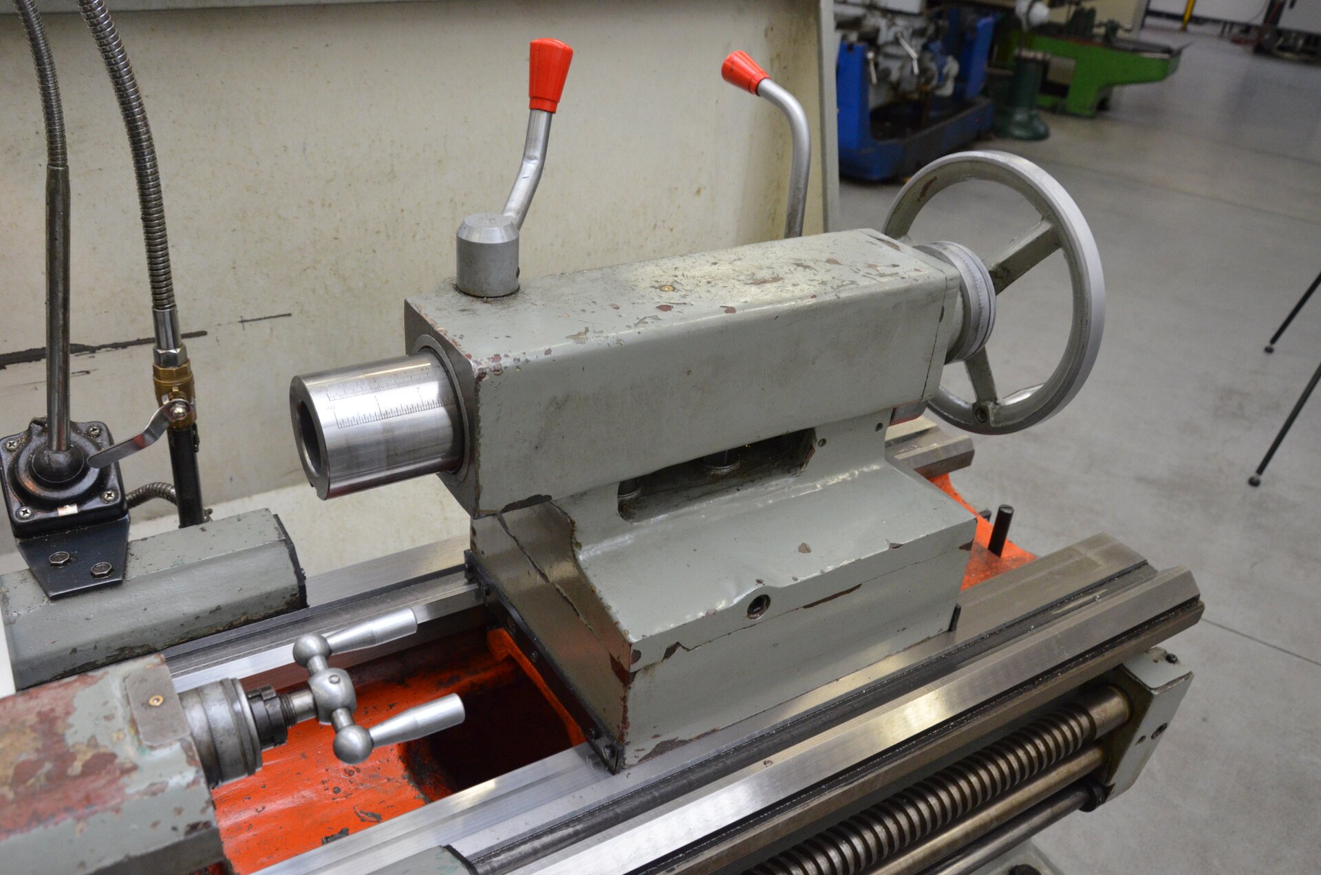 Ilustracja przedstawia konik tokarski. Konik zbudowany jest z tulei wysuwnej, dźwigni blokowania przesuwu, korpusu oraz pokrętła sterowania wysuwem tulei. Na korpusie znajdują się dwie wajchy z czerwonymi końcówkami. 