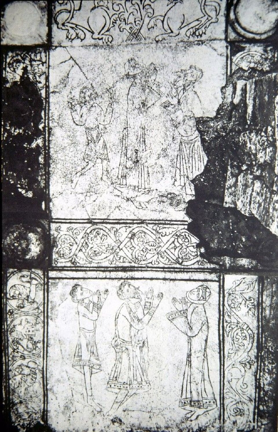 Ilustracja o kształcie pionowego prostokąta przedstawia czarno‑białą fotografię gipsowej płyty z krypty kolegiaty w Wiślicy. Płyta podzielona jest na dwie części. Ukazuje adorantów podczas modlitwy, zgrupowanych po trzech w każdym polu. Pola otoczone są dekoracyjną bordiurą. Po bokach widoczne są zniszczenia płyty w postaci czarnych plam. 