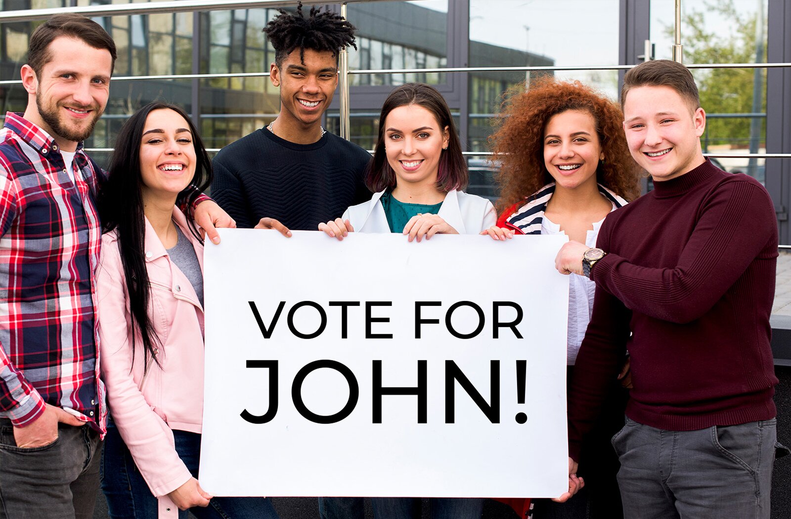 Zdjęcie przedstawia grupę sześciu młodych ludzi stojących frontalnie i trzymających białą tablicę z napisem w języku angielskim: VOTE FOR JOHN!, zapisanym czarnymi literami.  Od lewej widoczny jest mężczyzna z ciemnymi włosami, ubrany w koszulę w kratę. Obok niego stoi dziewczyna z długimi, ciemnymi włosami, ubrana w różową kurtkę. Kolejny jest chłopak z kręconymi, czarnymi włosami, noszący czarny sweter. Następnie dziewczyna z półdługimi, ciemnymi włosami, ubrana w zieloną bluzkę i białą bluzę. Obok niej stoi dziewczyna z długimi, kręconymi rudymi włosami, ubrana w białą bluzkę. Po prawej stronie grupy znajduje się chłopak z krótkimi, ciemnymi włosami, noszący bordowy sweter.  Wszyscy są uśmiechnięci.