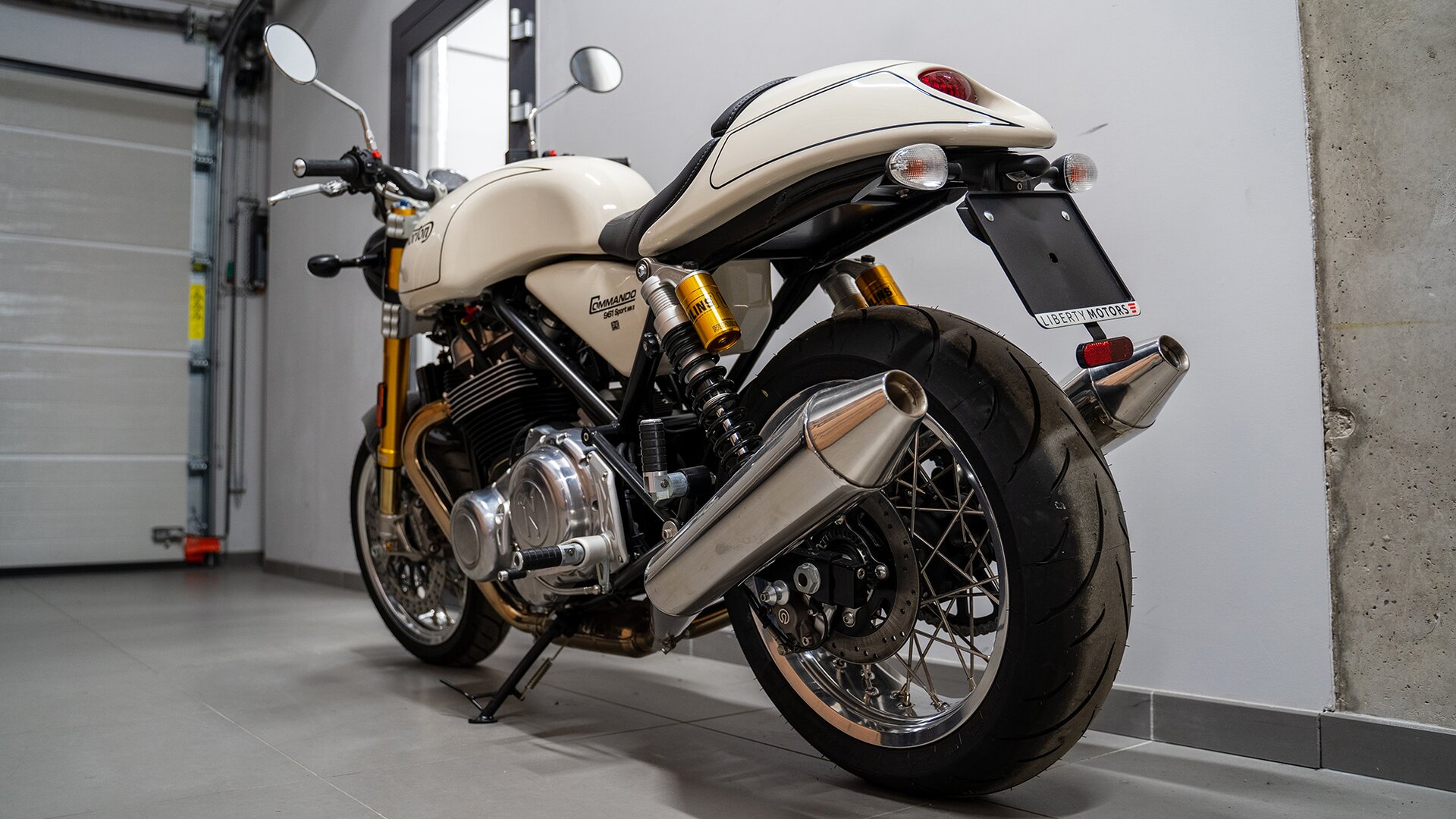 Zdjęcie przedstawia model motocykla Norton Commando 961 Sport MK2. Motocykl ma chromowane elementy, między innymi okrągłe przednie lusterka, obudowa baku, karoseria za siedzeniem oraz pod siedzeniem są koloru jasnobeżowego. Motocykl jest ukazany od tyłu.   