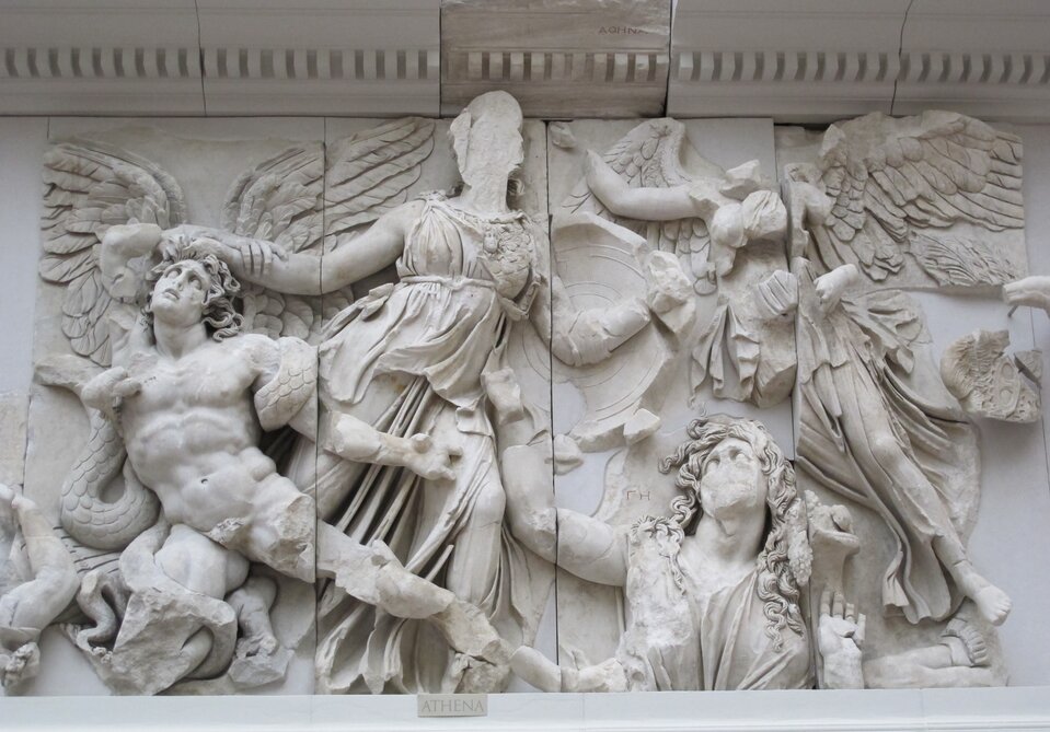 Ilustracja przedstawia fragment płaskorzeźby „Atena, Gaja i Nike” z II wieku p.n.e., znajdującej się w Muzeum Pergamońskim w Berlinie. W centrum widoczna jest potężna postać Ateny ukazana w dynamicznym ruchu, z rozwianymi fałdami szat i wyciągniętym ramieniem chwytającym skrzydlatego przeciwnika. Po jej lewej stronie znajduje się wynurzająca się z ziemi Gaja, przedstawiona jako kobieca postać o pełnych kształtach, zwrócona ku Atenie w geście błagania. Po prawej stronie unosi się drobniejsza, skrzydlata Nike, jakby wspierająca boginię w walce. W tle i u dołu widoczne są fragmenty innych postaci, częściowo uszkodzonych, co podkreśla dramatyzm sceny. Całość wyrzeźbiona jest w marmurze z niezwykłą dbałością o detale: napięte mięśnie, ruch tkanin i ekspresję twarzy.