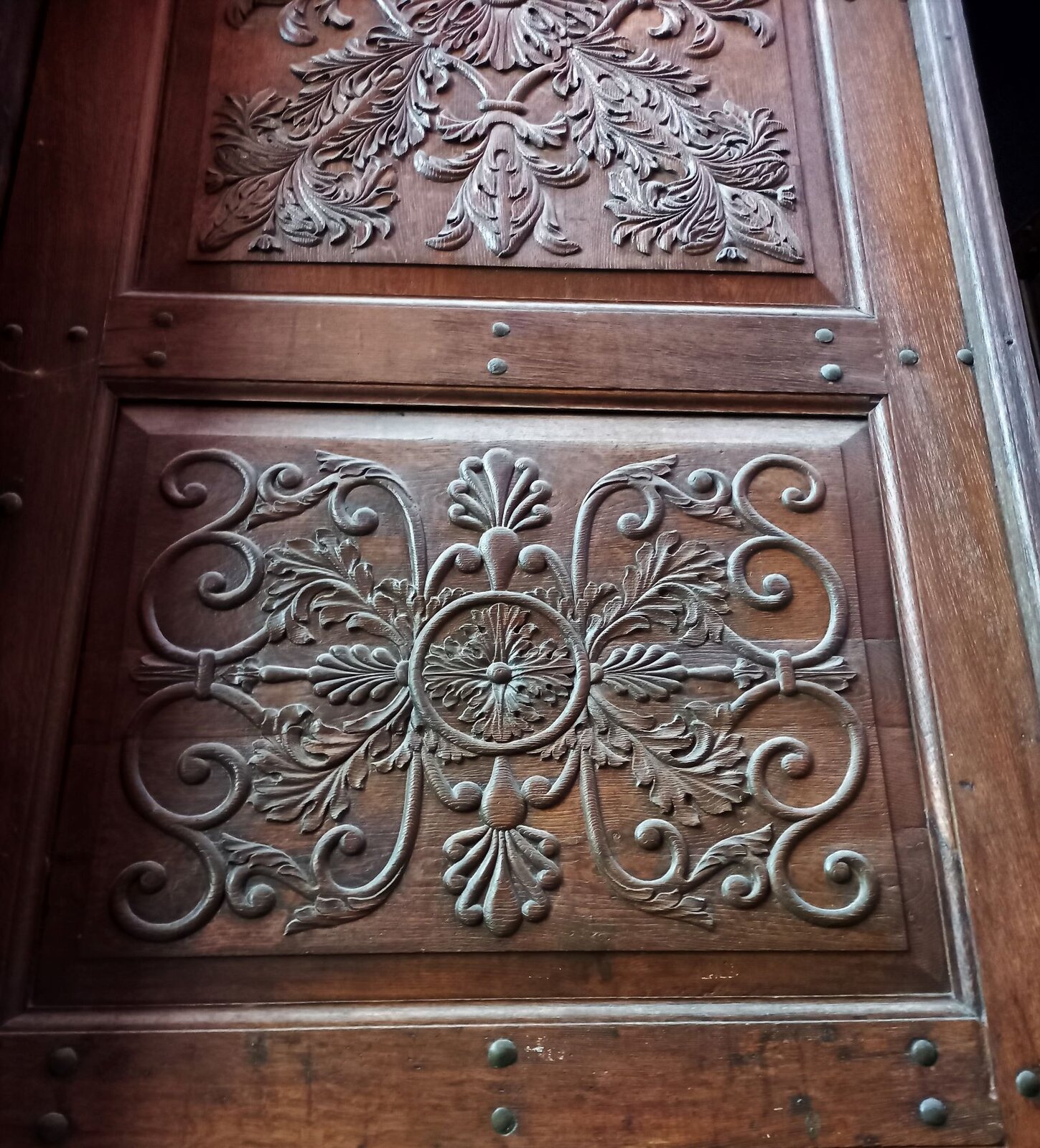 Zdjęcie przedstawia fragment dekoracji snycerskiej drewnianych drzwi kościelnych. Podzielone są na kwadraty, w środku których zostały wykonane dekoracyjne płaskorzeźby z motywem roślinnym.   