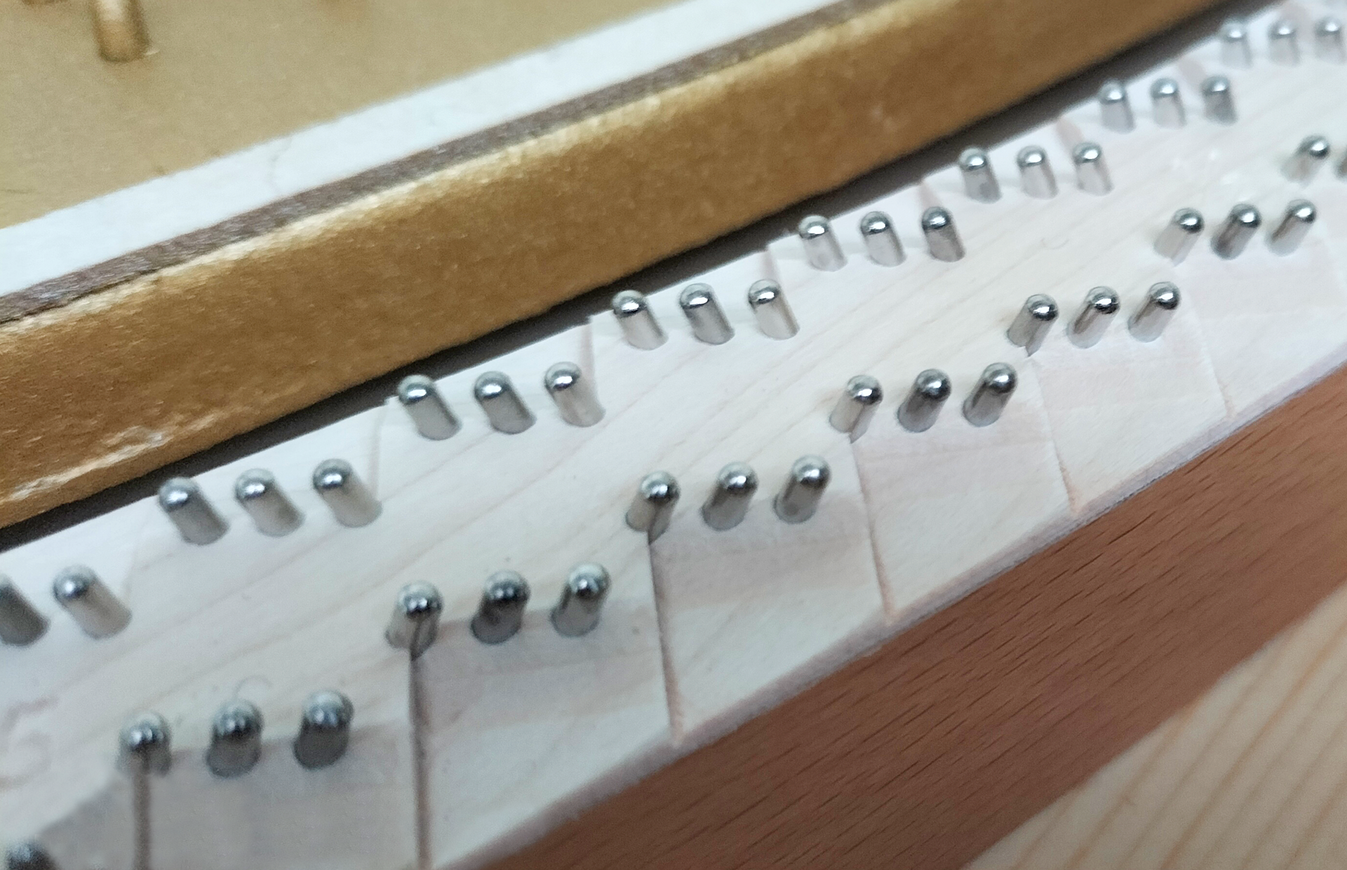 Zdjęcie przedstawia kołki mostkowe ze stali niklowanej. Widoczne są dwa rzędy kołków, wbite po trzy w biały prostokątny pas.