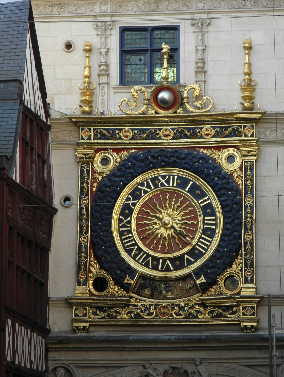 Ilustracja przedstawia zegar naścienny. Jest w kolorach granatu i złota. Ma prostokątną ramę z bogatymi zdobieniami w kształcie słupków, oraz chińskich smoków. W środku zegara znajduje się słońce.