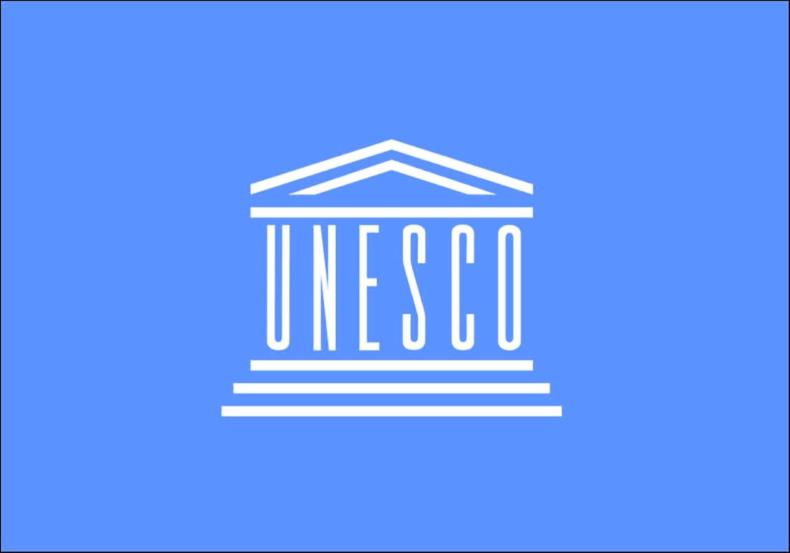 Ilustracja przedstawia znak Międzynarodowej Organizacji UNESCO  , zajmującej się ochroną dziedzictwa kulturowego na świecie. Znak składa się z nazwy  UNESCO  napisanej prostymi, wielkimi literami. Napis jest przykryty dachem w kształcie trójkąta, pod nim poziome linie oznaczają schody. Całość przypomina starożytną budowlę. 