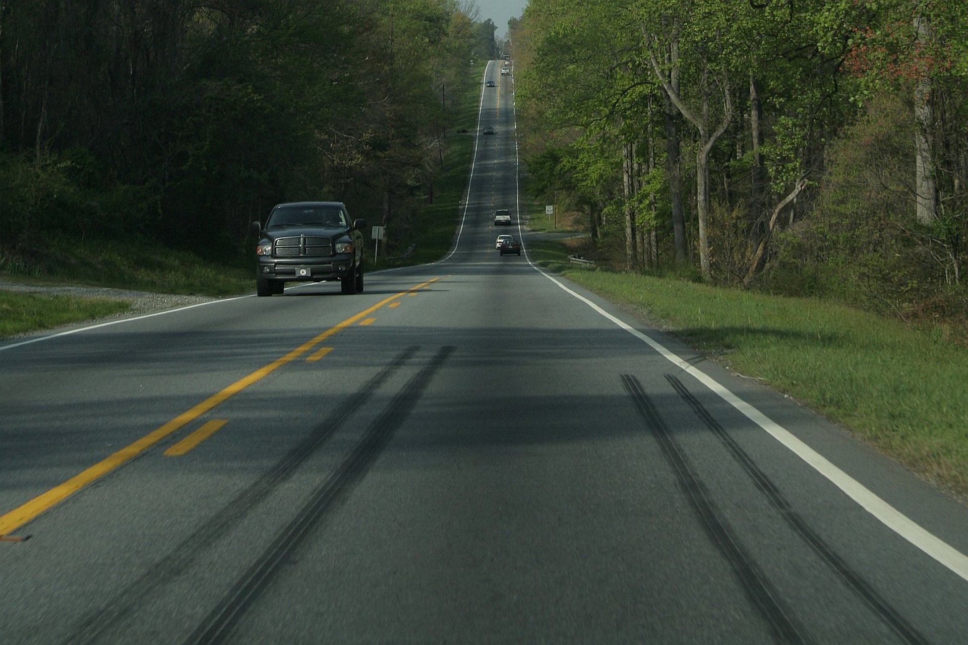 Zdjęcie przedstawia drogę z jadącymi samochodami z wysokim wzniesieniem w tle, aparat znajduje się nisko nad asfaltem. Na pierwszym planie na asfalcie widać ślady po bardzo ostrym hamowaniu.