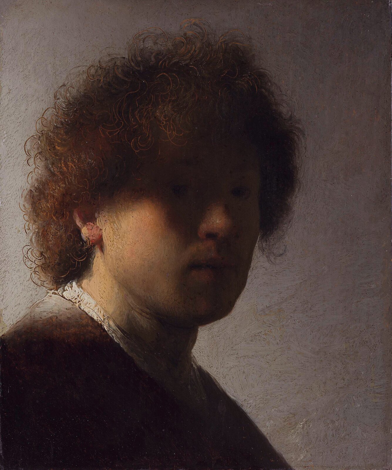Ilustracja przedstawia "Autoportret" Rembrandta określany jako z zacienioną twarzą. Ukazuje młodego mężczyznę z lokowanymi, brązowymi włosami. Światło pada z lewej strony, rozjaśniając część twarzy artysty. Prawa strona jest ukryta w cieniu. Malarz zadbał o detale – szczegółowo oddał loki na głowie. Jednolite tło, utrzymane w szarościach kontrastuje z postacią i eksponuje twarz.