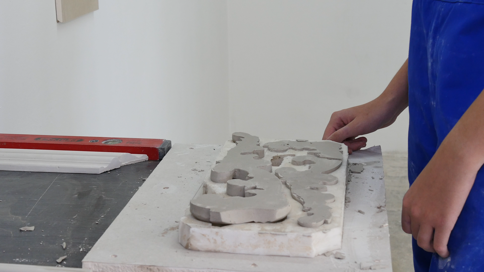 Zdjęcie przedstawia elastyczną formę do wykonywania modeli detalu architektonicznego. Forma składa się z mniejszych fragmentów, które są rozłożone na kamiennej płaszczyźnie na stole. Obok stołu znajduje się pracownik w stroju roboczym.