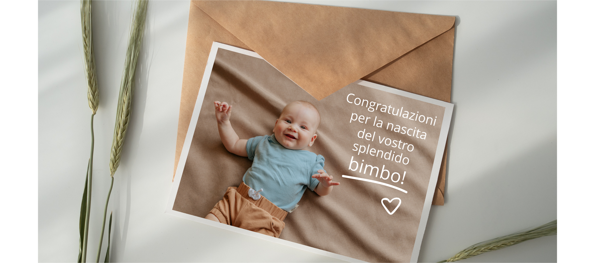 Zdjęcie wykonane z góry przedstawia kartkę z życzeniami. Na kartce znajduje się zdjęcie niemowlaka, który leży na plecach. Obok dziecka na kartce znajduje się napis: Congratulazioni per la nascita del vostro splendido bimbo!  Kartka leży na kopercie. Po lewej stronie widoczne są dwa kłosy zboża.