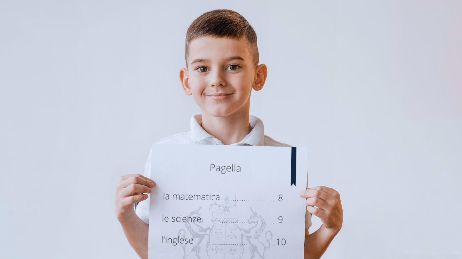 Zdjęcie przedstawia nastoletniego chłopca z krótkimi włosami, który trzyma w rękach kartkę, na której znajdują się oceny. Na świadectwie znajduje się tekst: "Pagella. la matematica 8, le scienze 9, l'ingese 10".