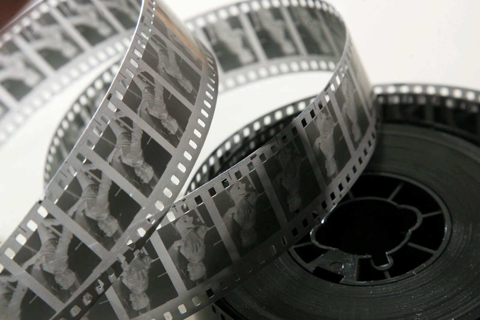 Zdjęcie przedstawia kliszę - film negatywowy 35mm, na dużej szpuli, częściowo rozwinięty. Da się na nim zauważyć pojedyncze klatki z postacią. Dawniej na takiej kliszy rejestrowano filmy. 