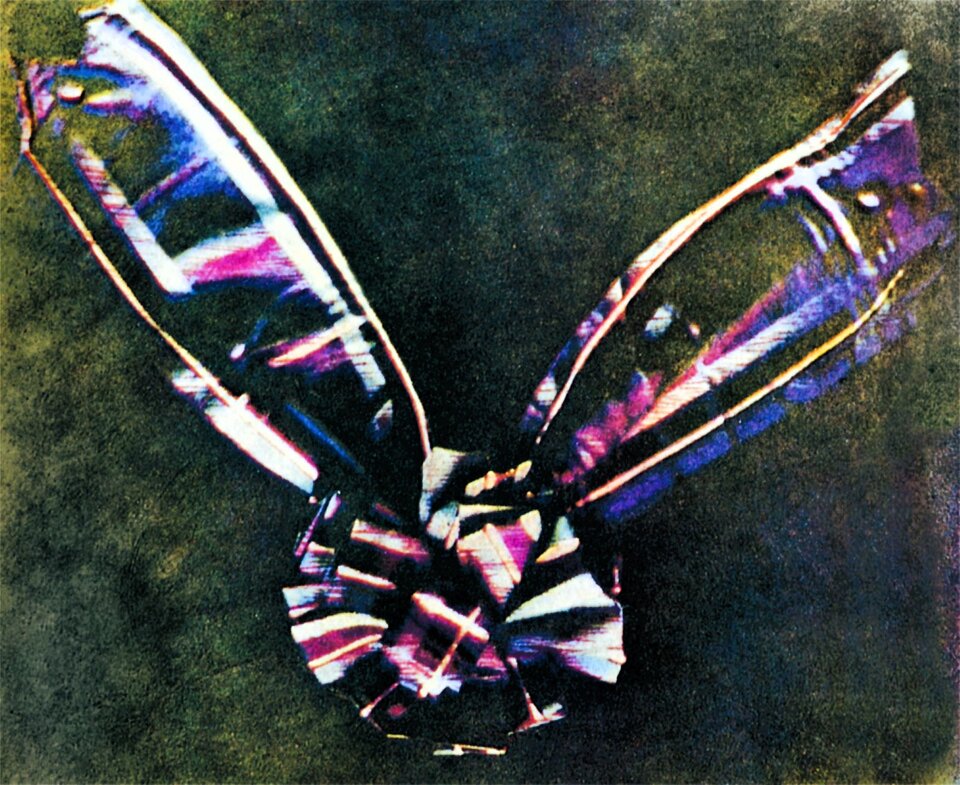 Ilustracja przedstawia fotografię. W centrum kadru, na dole znajduje się koło. W górnej jego części, niemal symetrycznie położone znajdują się dwie podłużne owalne formy. Elementy są w podobnych kolorach. Tło jest zielone.