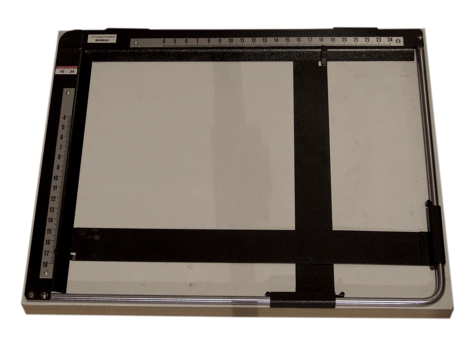 Zdjęcie przedstawia maskownicę, Widoczny jest prostokątny biały przedmiot, na którego lewym i górnym boku znajdują się dwie podziałki centymetrowe, zaś w lewym dolnym narożniku krzyżują się dwie taśmowate czarne linie.