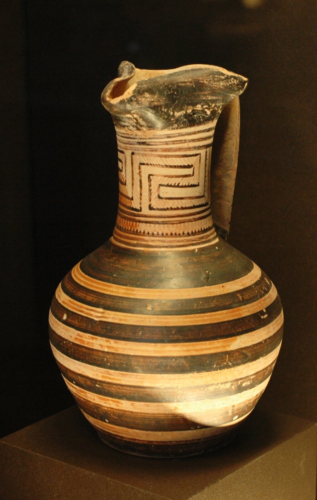 Na zdjęciu przedstawiona została waza czerwonofigurowa. Na czarnym tle namalowane zostały jasne pasy; szyjkę naczynia zdobią motywy geometryczne.