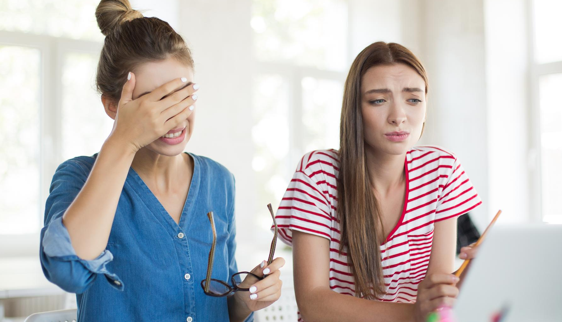 Zdjęcie przedstawia dwie dziewczyny, w ujęciu od pasa w górę. Dziewczyna po lewej stronie ma blond włosy upięte w kok, jest ubrana w jeansową koszulę. W lewej ręce trzyma okulary korekcyjne, zaś prawą dłonią zakrywa twarz. Dziewczyna po prawej ma długie, rozpuszczone blond włosy i jest ubrana w bluzkę z krótkim rękawem w biało‑czerwone paski. Ma zatroskaną twarz.