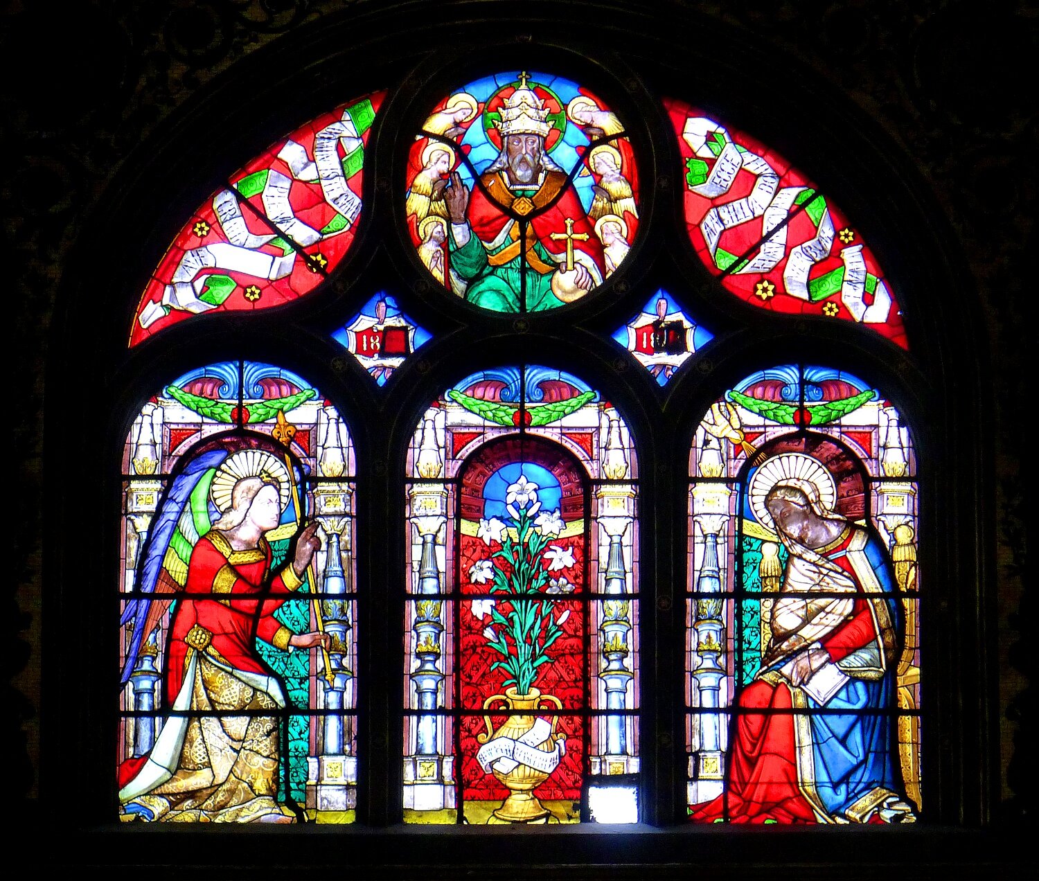 Na zdjęciu okno i witraż w kościele św. Eustachego w Paryżu. Maswerk łukowaty zakończony okrągłym kształtem. Na witrażu dziewięć postaci. Trzy główne, sześć pobocznych. 