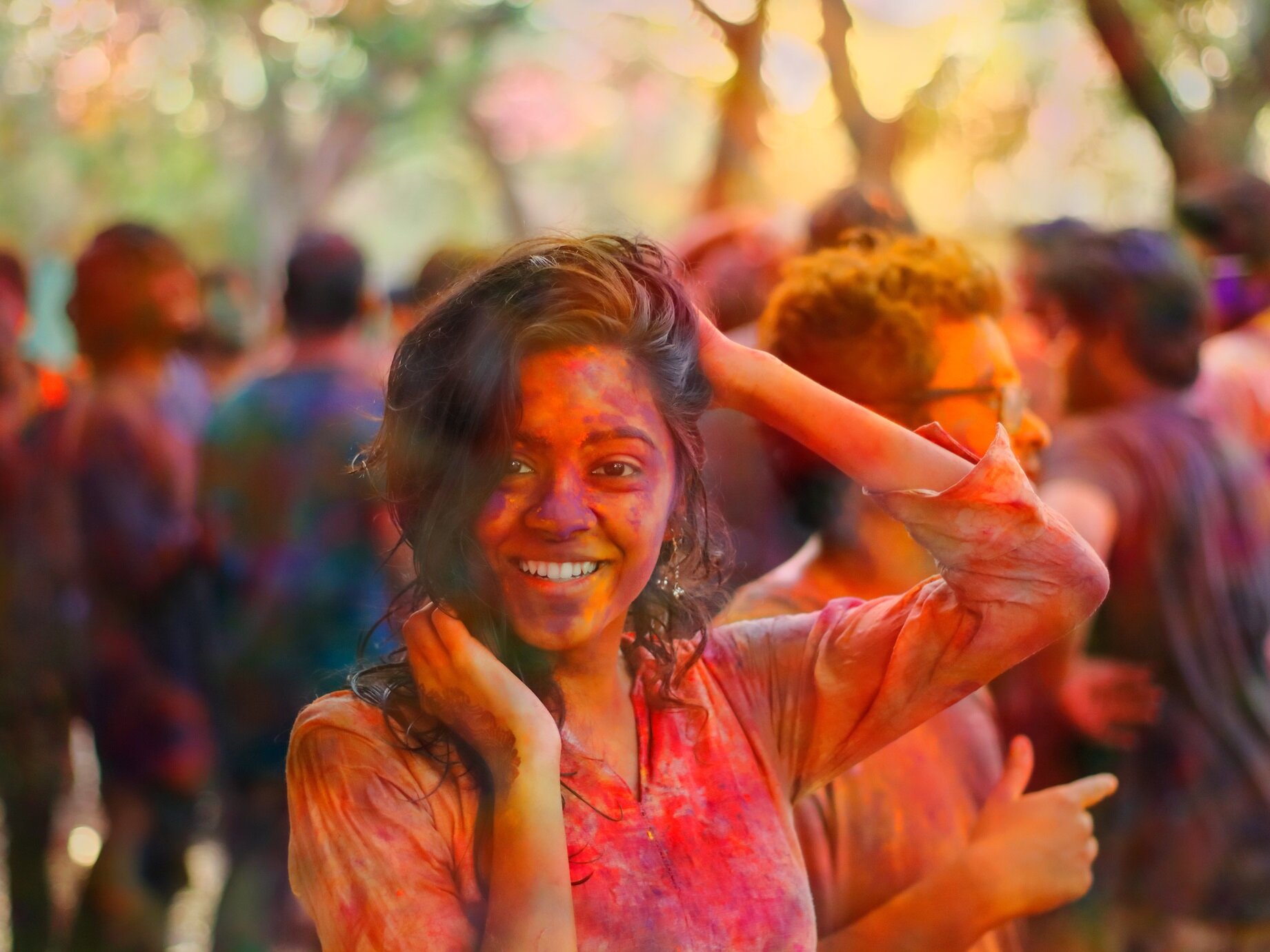 Zdjęcie przedstawia młodą, uśmiechnięta kobietę całą w kolorowym pyle. W tle za nią ukazano tłum ludzi, którzy również są kolorowo ubrudzeni.