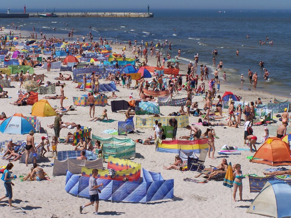 Na zdjęciu jest zatłoczona plaza latem. W tle widać molo. 