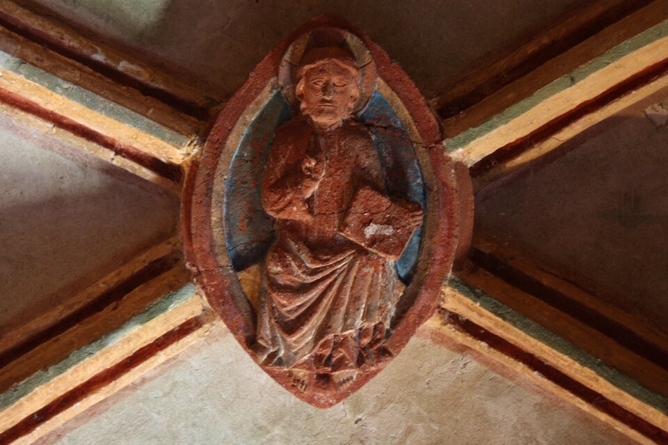 Ilustracja przedstawiająca zwornik, na którym widoczna jest postać świętego z aureolą trzymającego książkę. Święty ubrany jest w szaty.