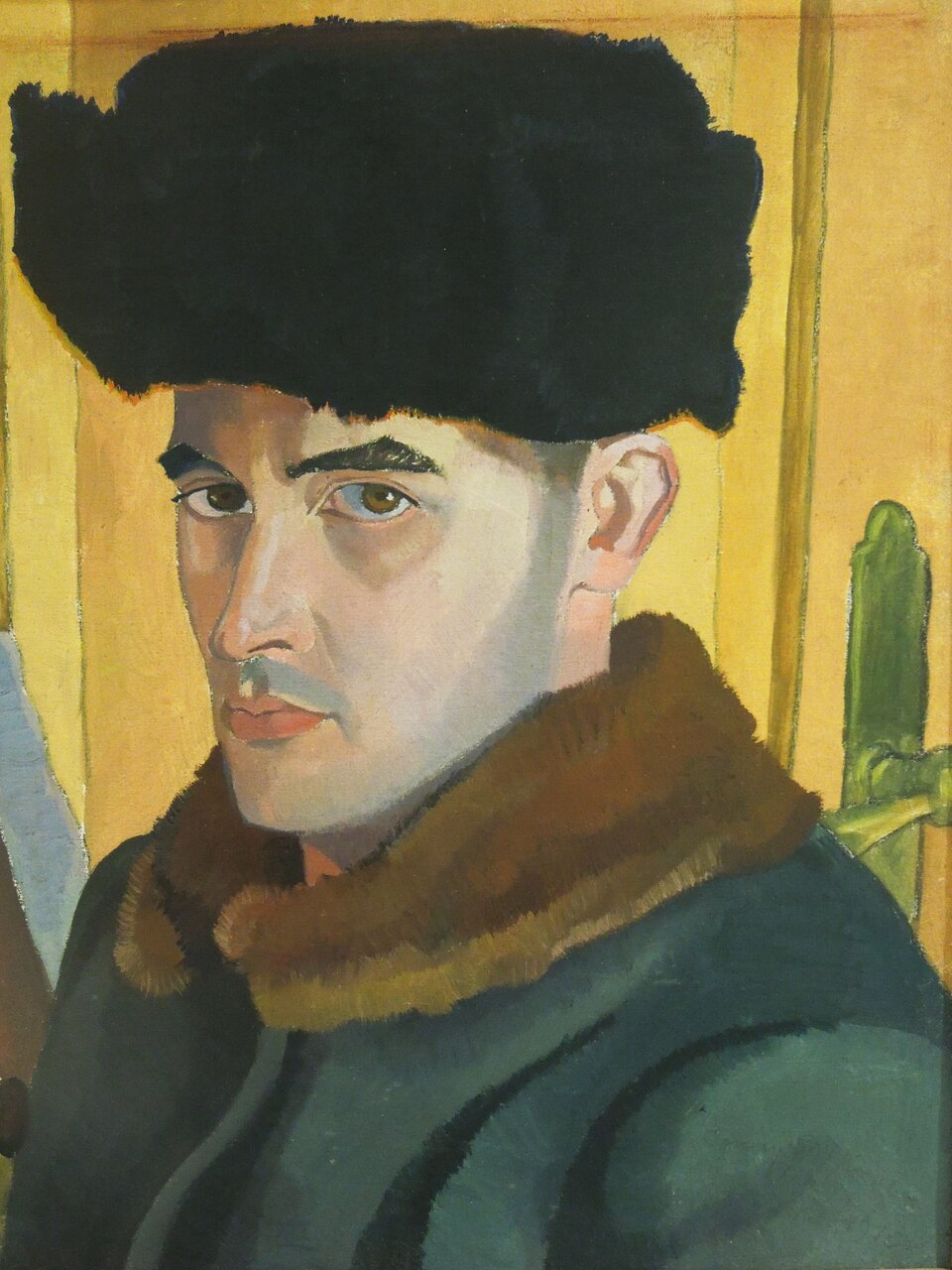 Obraz przedstawia mężczyznę. Ma on pociągłą twarz oraz lekki zarost, brązowe oczy i prosty nos. Na głowie ma założoną czarną puchatą czapkę. Jest ubrany w gruby płaszcz. 