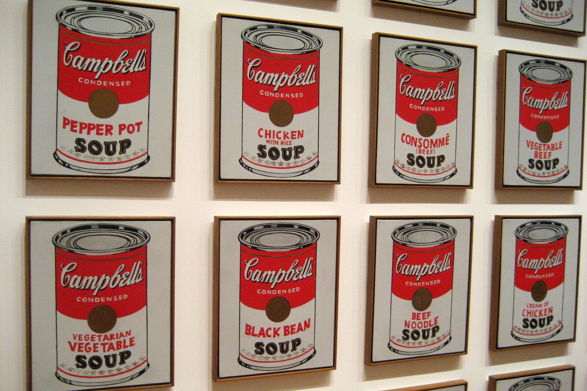 Zdjęcie przedstawia ścianę, na której zawieszone są w dwóch rzędach te same obrazy z Campbell's Soup I. Obrazy przedstawiają puszkę z czerwono‑białą nalepką i napisem Campbell's Condensed Vegatarian Vegetable Soup.