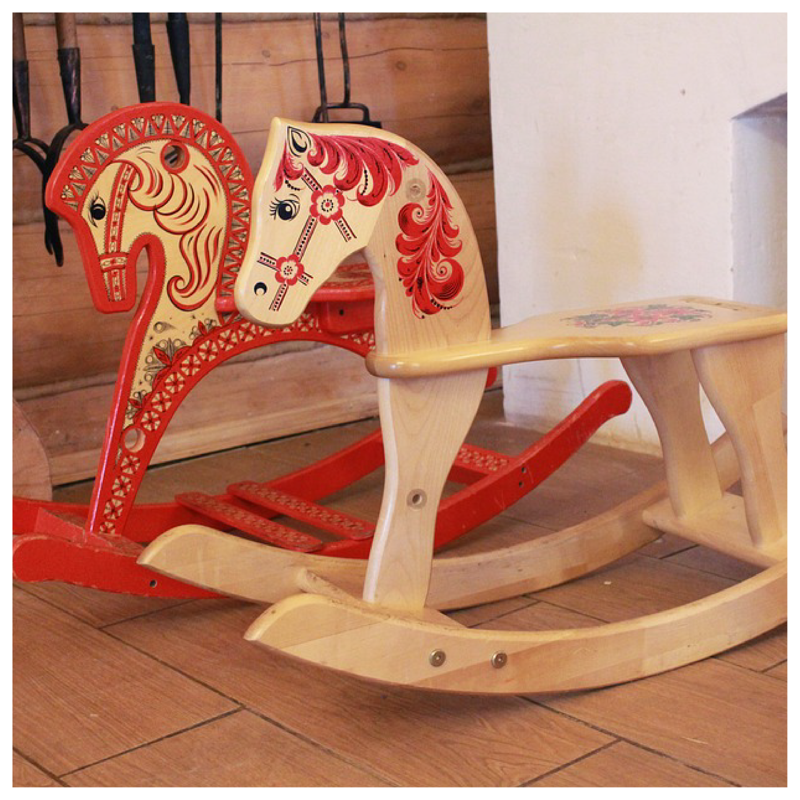 Zdjęcie przedstawia dwa drewniane konie na biegunach z czerwono‑czarnymi ozdobami.