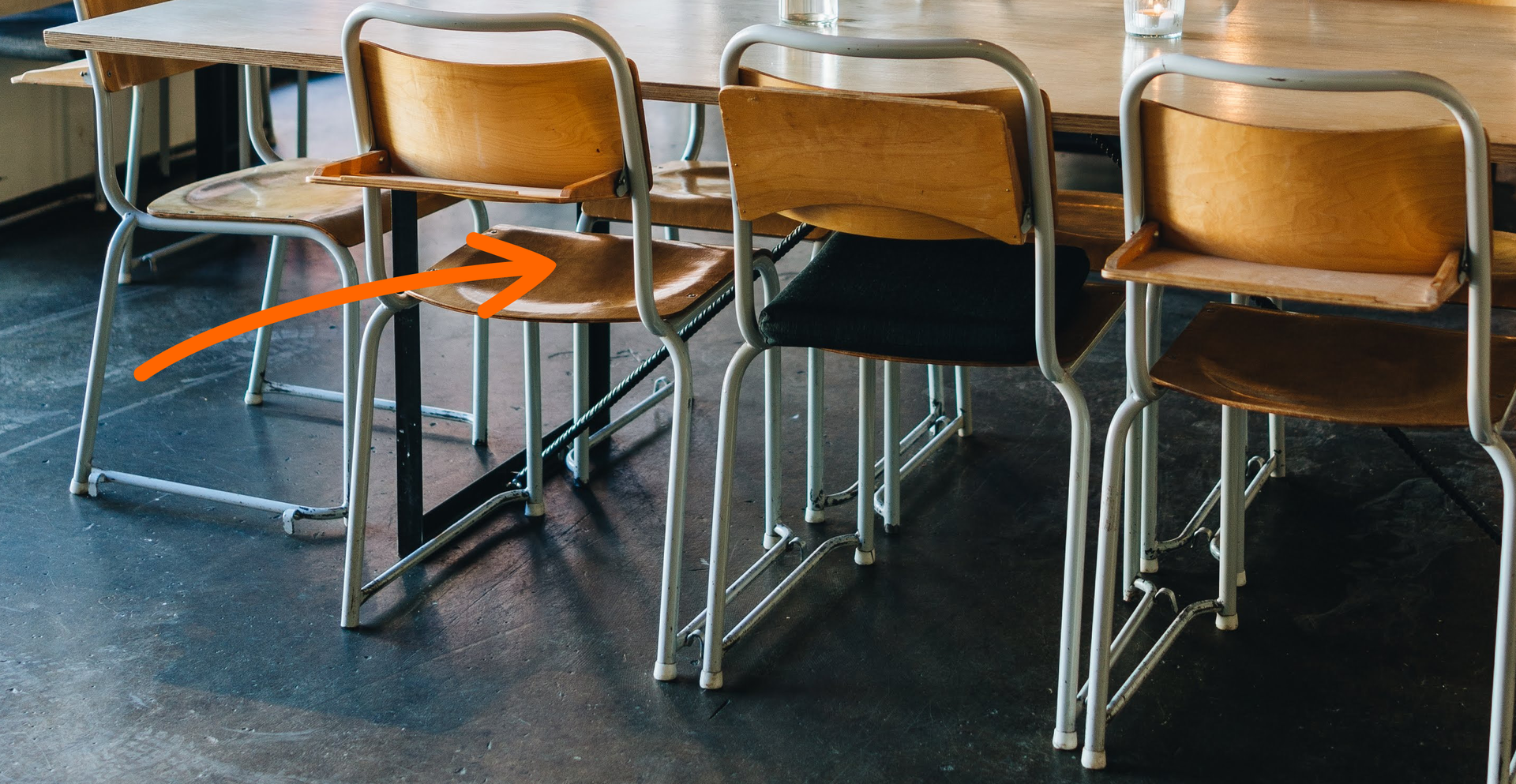 Zdjęcie przedstawia krzesła stojące przy stole. Strzałka skierowana jest na krzesło.