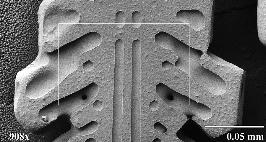 Zdjęcie mikroskopowe przedstawia zbliżenie dziewięćsetośmiokrotne na kryształ śniegu. Widoczne są kształtne żłobienia w ramieniu gwiazdy kryształu śniegu.