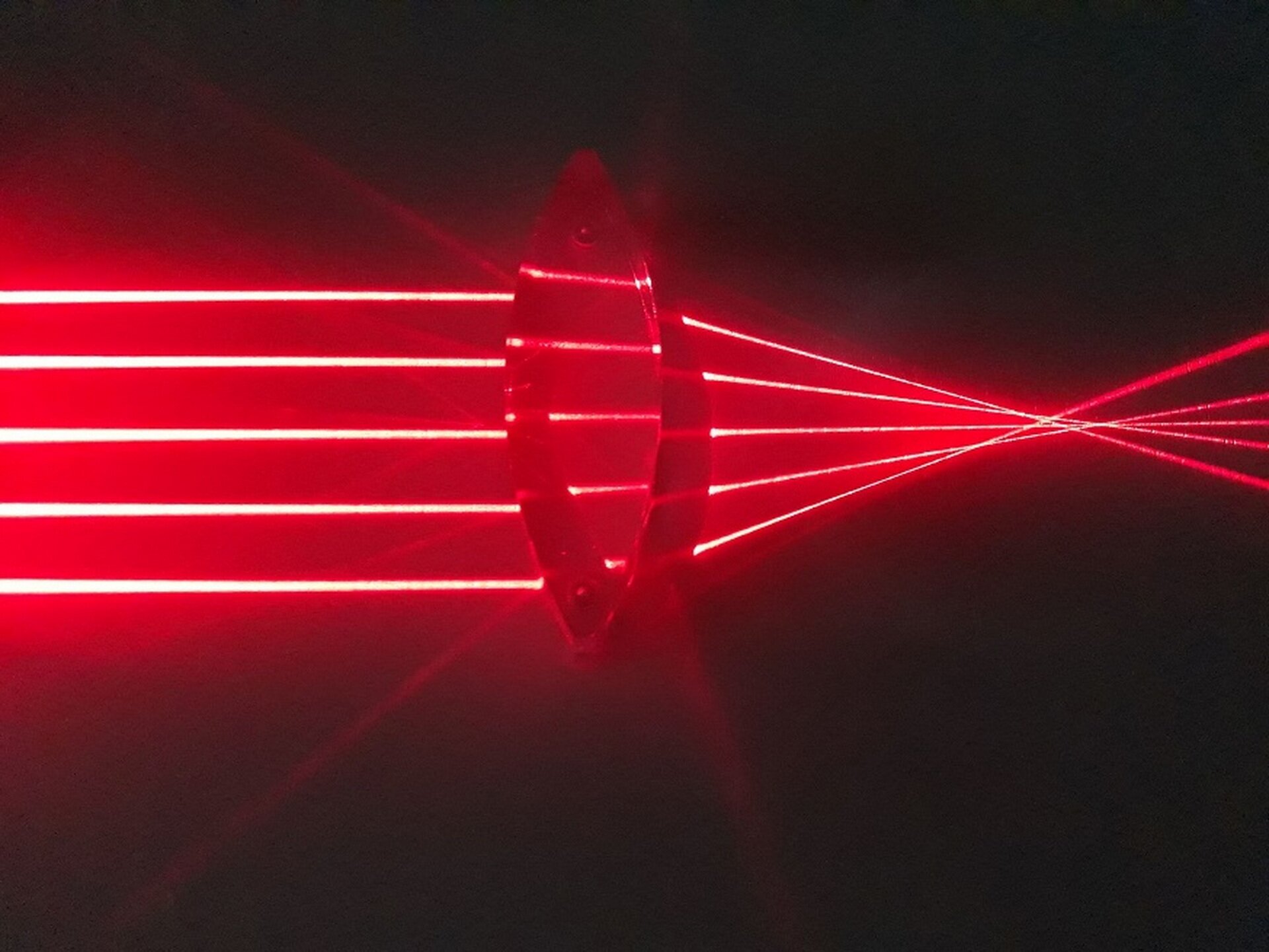 Na zdjęciu prezentowany jest bieg promieni przechodzących przez soczewkę skupiającą. Z lewej strony soczewki widoczne jest pięć czerwonych promieni równoległych do siebie i równo od siebie odsuniętych. Wiązka tych promieni pada na soczewkę dwuwypukłą, znajdującą się na środku obrazu. Wewnątrz materiału obserwujemy ugięcie wiązki promieni, natomiast po wyjściu z soczewki, po jej prawej stronie, promienie biegną jeszcze bardziej ugięte, aż do miejsca, w którym się całkowicie wszystkie przecinają. W rezultacie promienie odtworzą rzeczywisty przedmiot w postaci obrazu utworzonego z punktów przecięcia się promieni, który będzie powiększony i odwrócony. 