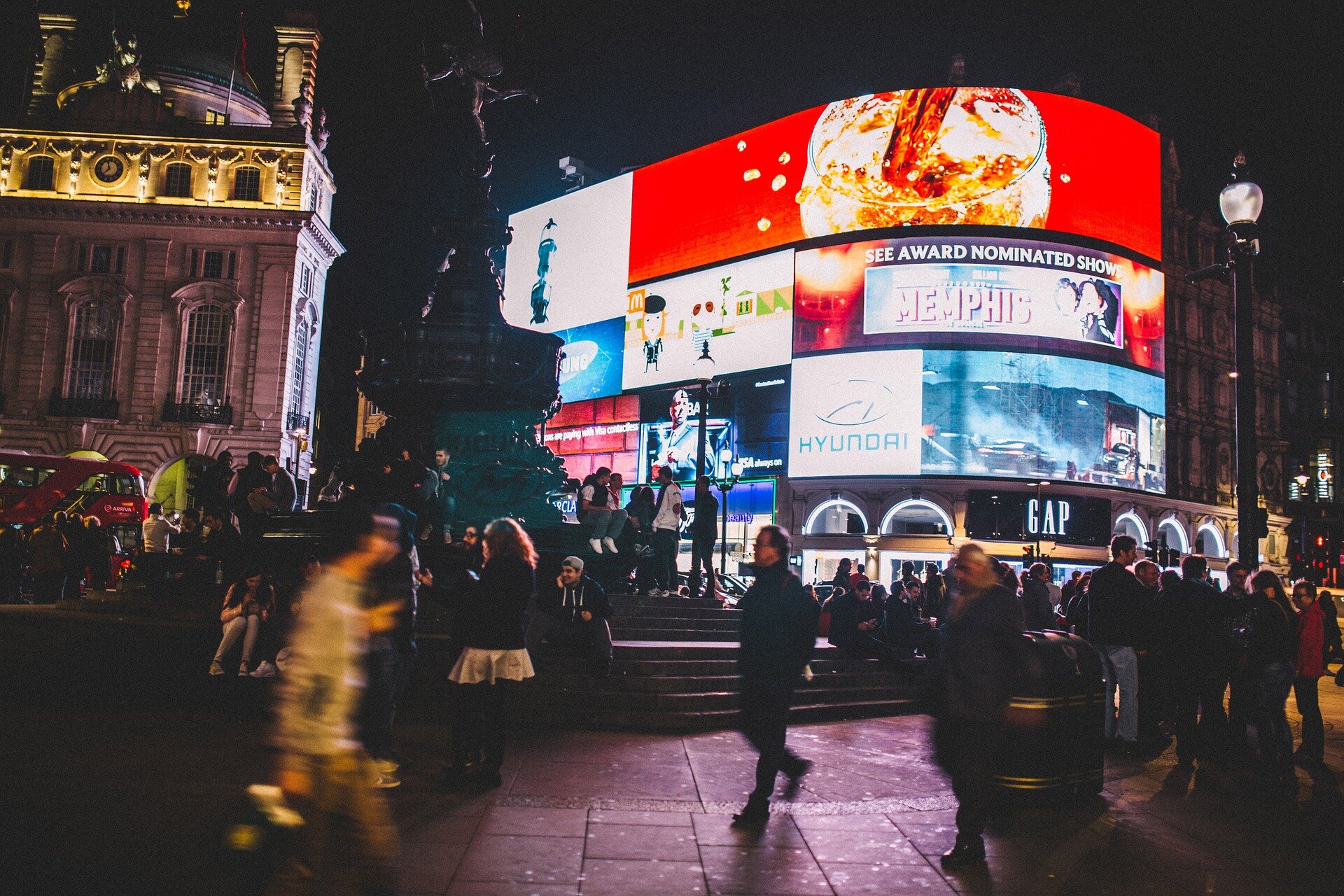 Zdjęcie przedstawia londyński Picadilly Circus. Na placu znajdują się tłumy ludzi. Przy placu stoi budynek, na którym znajduje się wiele ekranów. Widoczne są na nich reklamy: Coca‑coli, Hyundaia. Jest także reklama uroczystości rozdania nagród w Memphis.