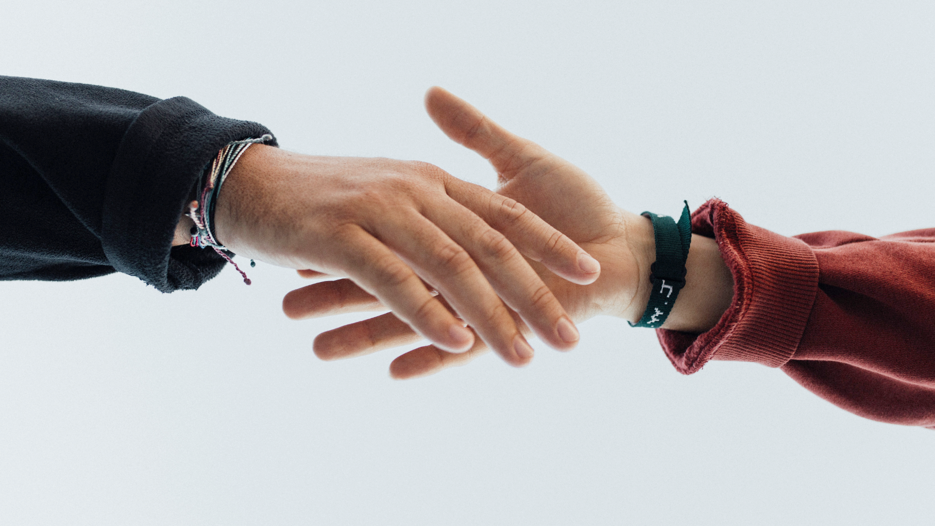 Zdjęcie przedstawia zbliżenie na ręce dwóch osób podających sobie dłonie. Obie osoby mają na nadgarstkach bransoletki.