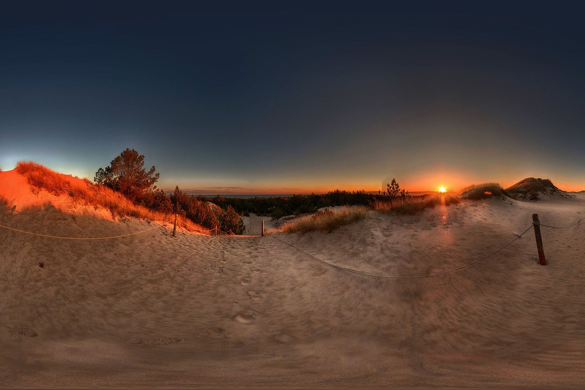 Zdjęcie przedstawia Słowiański Park Narodowy. Znajduje się na nim, wyznaczone ogrodzeniem ze sznurów, przejście na brzeg morza przez piaszczyste wydmy.
