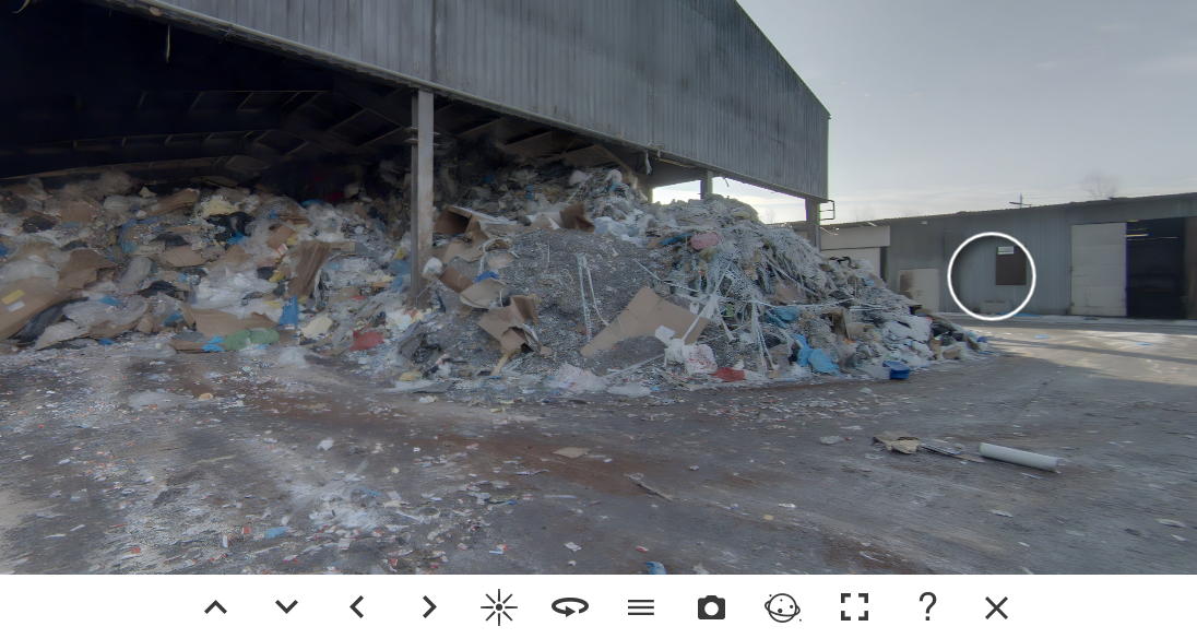 Grafika przedstawia ekran wycieczki wirtualnej. Znajduje się tu kadr filmu przedstawiający składowisko odpadów. Pod kadrem znajduje się w dolnym panelu pasek menu z przyciskami umożliwiającymi nawigowanie po wycieczce.