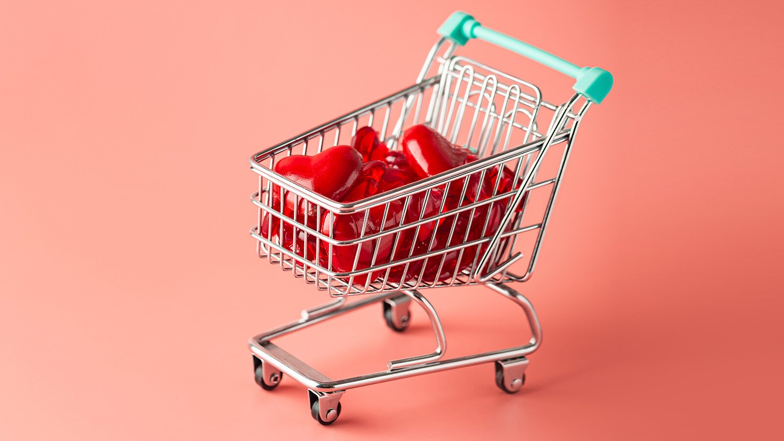 Zdjęcie przedstawia miniaturowy wózek sklepowy, który jest wypełniony czerwonym serduszkami. 