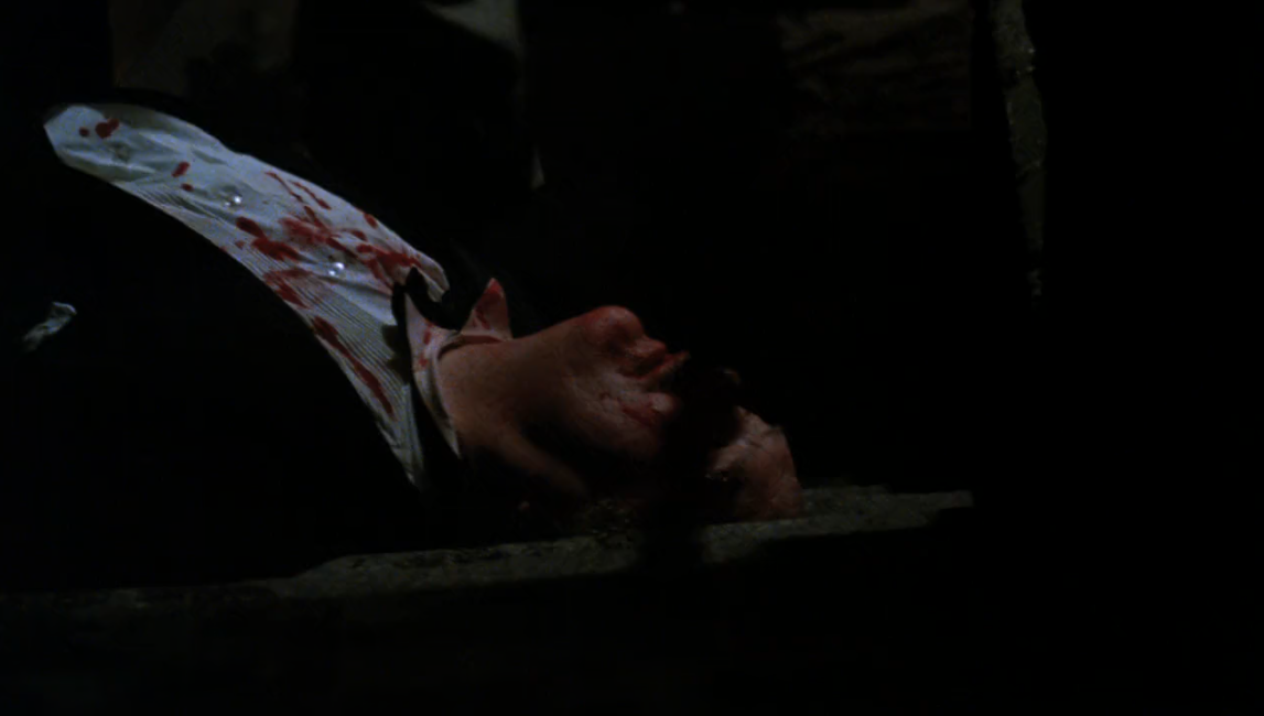 Zdjęcie przedstawia leżącego mężczyznę w garniturze z zakrwawioną twarzą.