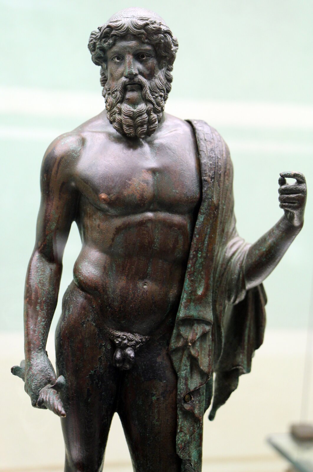 Fotografia przedstawia rzeźbę nieznanego autorstwa pod tytułem „Zeus przedstawiony z piorunem”. Zeus został przedstawiony jako półnagi stojący mężczyzna w średnim wieku. Grecki bóg ma atletyczna budowę ciała, bujny zarost i włosy. Przez bark ma przerzuconą szatę. Jedną rękę ma podniesioną do góry, w drugiej trzyma piorun. Figura jest koloru brązowego.