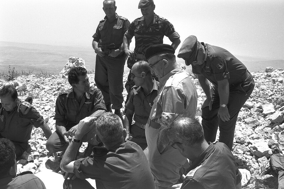 Zdjęcie przedstawia grupę wojskowych. Rozmawiają, znajdują się na kamienistym wzniesieniu. Część żołnierzy siedzi, trzech z nich stoi.     