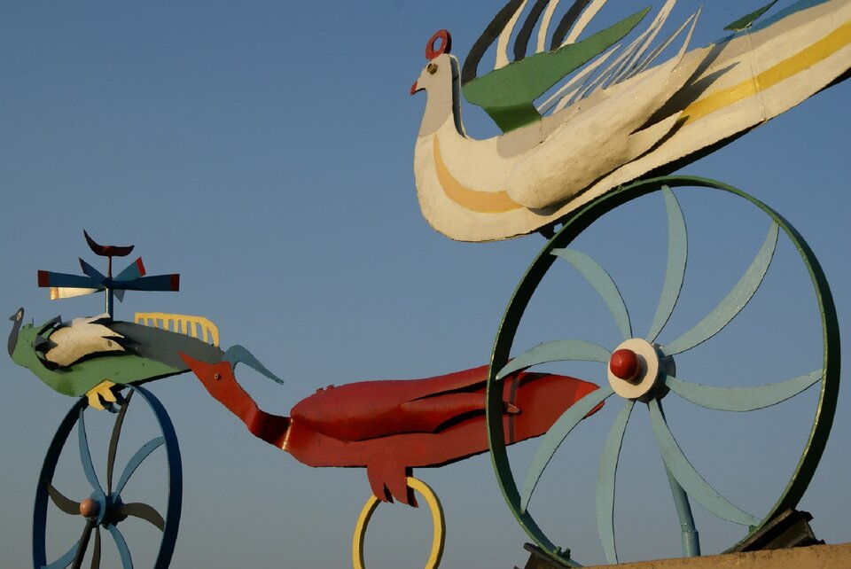 Fotografia przedstawiająca rzeźbę kolorowych ptaków osadzonych na ażurowych metalowych kołach róznej wielkości. Na fotografii widoczne są trzy ptaki.