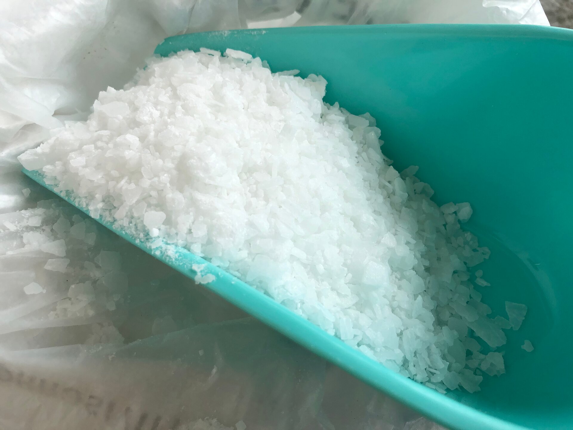 Slajd. Zdjęcie na slajdzie przedstawiające miętową łopatkę, na której znajduje się biała sól kamienna. Łopatka leży na białej folii.