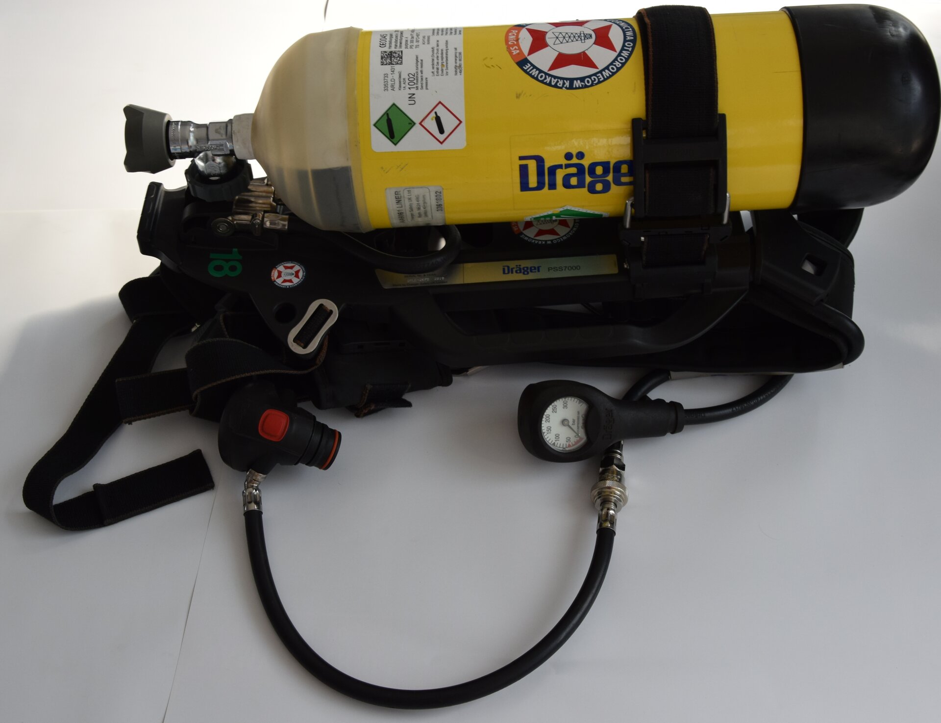  Na zdjęciu przedstawiono zestaw aparatu oddechowego ratownika. W centralnej części butli widoczna jest żółta butla o kształcie cylindra. W górnej części butli widoczny jest zawór. Butla znajduje się na czarnym stelażu. Po obwodzie zapięta jest pasem. Z boku butli odchodzi wężyk. Na końcu wężyka widoczny jest okrągły wskaźnik.Poniżej zdjęcia w prawym dolnym rogu widoczny jest przycisk odtwarzania. Tekst nagrania jest zgodny z tytułem zdjęcia.